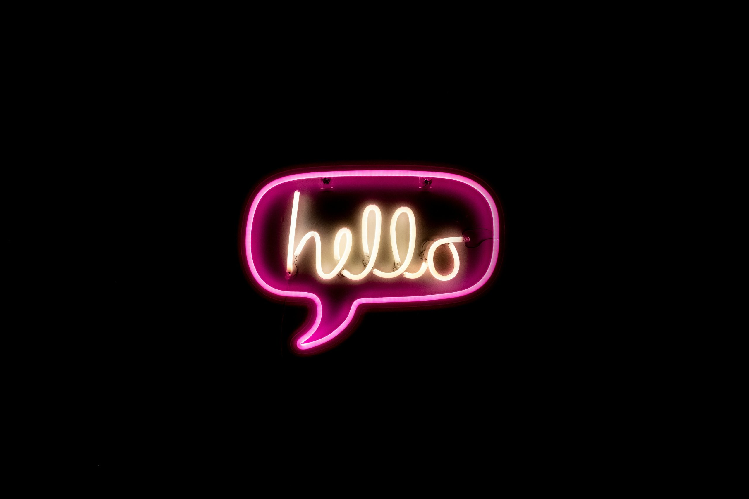 A pink and yellow neon speech bubble which says 'hello' against a black background.